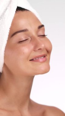 Beyaz havluyla beyaz bir kadın pürüzsüz, parlak bir ten ve cilt bakımından sonra kendine güvenen bir gülümseme sergiliyor. Güzellik ürünleri reklamları, kişisel bakım reklamları ve markalaşma için mükemmel..