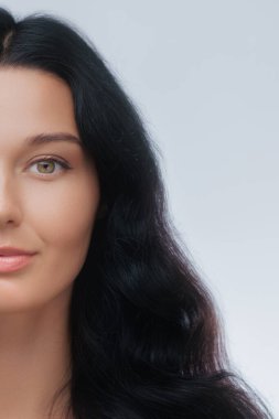 Minimalist yakın plan, pürüzsüz tenli ve parlak siyah saçlı bir kadının yüzünün yarısını gösteriyor. Kozmetik, saç bakımı, cilt bakımı veya fotokopi veya logo için alanı olan modern güzellik kampanyaları için idealdir..