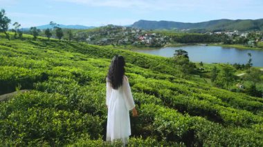 Beyaz giysili Asyalı bir kadının Gregory Gölü ve uzak tepelerle çay teraslarında gezindiği görüntüler. Seyahat reklamları, sağlık ve yaşam tarzı görselleri için ideal..