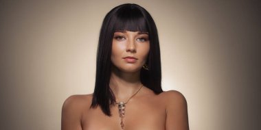 Sade siyah saçlı, zarif makyajlı ve bej arka planda altın mücevherli sofistike bir kadının portresi. Güzellik kampanyaları, moda makaleleri ve lüks marka promosyonları için mükemmel..