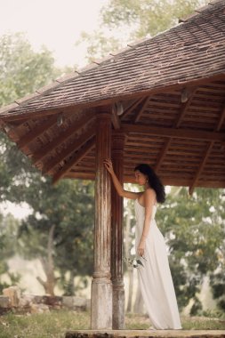 Beyaz pileli yaz elbisesi içindeki zarif beyaz kadın kırsal bir çardağın altındaki eski bir sütuna dokunuyor. Güzellik, kaplıca, moda ve romantik yaşam tarzı reklamları için mükemmel..