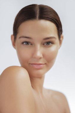 Kusursuz, parlak bir teni ve pürüzsüz sırt kılları olan, kameraya özgüvenle bakan beyaz bir kadının yüksek kaliteli portresi. Cilt bakımı, kozmetik ve sağlık kavramı