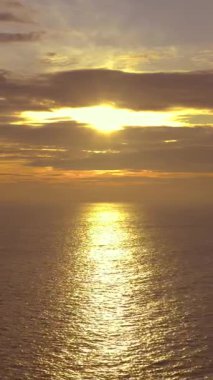 Sakin, sakin bir günbatımının sakin, sakin bir denizin üzerine yansıyan altın yansımalarını gösteren dikey drone videosu. Arka plan görselleri, tatil köyü promosyonları veya Bali gibi tropikal bölgelerdeki romantik temalar için mükemmel.