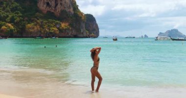 Bronzlaşmış bir kadın, tropik bir Tayland plajında sörf yaparken turkuaz suya ve ikonik teknelere bakıyor. Seyahat, moda, yaşam tarzı ve yaz tatili tanıtımları için ideal.