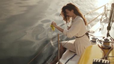 Yatta oturan beyaz elbiseli zarif bir kadın, altın gün batımının okyanusa yansıması gibi yavaşça suya yaprak batırıyor. Lüks seyahat, yaşam tarzı ve macera kampanyaları için mükemmel.. 