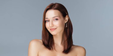 Düz kahverengi saçlı, yumuşak, parlak tenli, kendinden emin gülümseyen beyaz bir kadın. Yüksek kalite stüdyo güzellik çekimi kozmetik, cilt tanıtımı, moda ve yaşam tarzı kavramları için mükemmel..