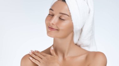 Parlak tenli barışçıl bir kadın kendini bir havluya sarar, gözlerini kapatır ve nazikçe gülümser. Rahatlamanın, güzelliğin vücut bulmuş hali, kendine özen göstermenin ve sağlığın tadını çıkarıyor.. 