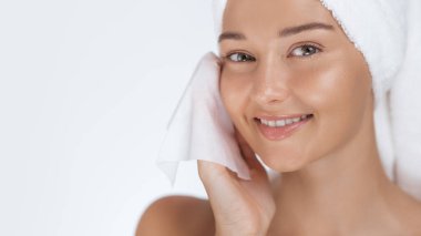 Yüzünü temizlemek için kozmetik mendil kullanırken ışıl ışıl gülümseyen güzel bir Asyalı kadın. Havluya sarılmış, kaliteli spa, cilt bakımı ve kozmetik tanıtımı için güzellik portresi konsepti.