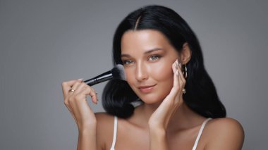 Kusursuz ciltli güzel bir kadın makyaj fırçasıyla toz sürüyor zarafet ve kendine güven saçıyor. Lüks güzellik kampanyaları ve cilt bakımları için ideal.. 