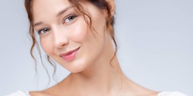 Kusursuz bir cildi ve minimum makyajı olan gülümseyen beyaz bir kadının stüdyo güzelliği portresi. Kozmetik endüstrisi reklamları, cilt bakımı kampanyaları, sağlık görselleri ve yaşam tarzı markalaşması için mükemmel..