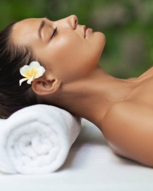 Lüks kaplıcalarda saçında tropik çiçeklerle masaj masasında yatan çekici bir kadın. Güzellik, kaplıca tedavisi, cilt bakımı, sağlık, tatil ve lüks yaşam tarzı için kavramsal stok görüntüleri