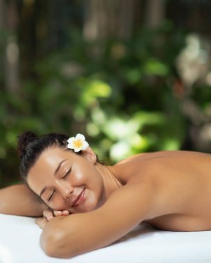 Genç beyaz kadın, lüks bir kaplıcada karnının üstünde dinleniyor, gözleri kapalı ve saçları Frangipani çiçeği gibi. Güzellik ve sağlık konsepti, cilt bakımı ve spa markaları için mükemmel..