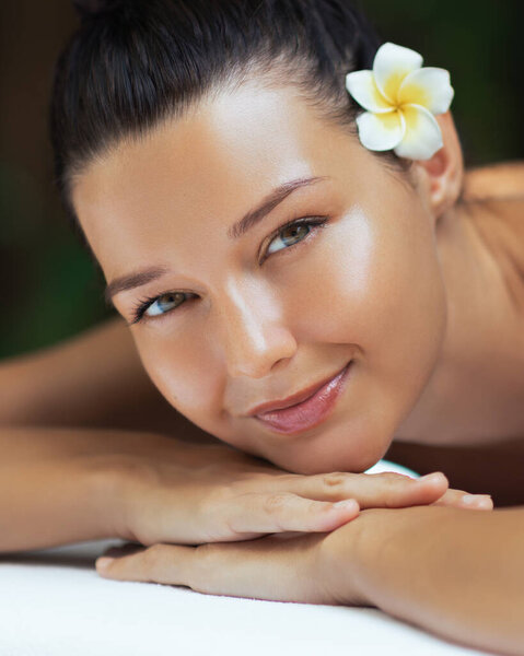 Beautiful young woman resting at spa with tropical flower in her hair and radiant skin. High quality conceptual footage for beauty, skincare, spa treatment, wellness, vacation, and luxury lifestyle