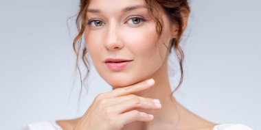 Beyaz dantelli bir elbise içindeki parlak ciltli ve zarif makyajlı genç bir kadının yumuşak stüdyo portresi. Cilt bakımı, moda, gelin ve minimalist güzellik markası için mükemmel..