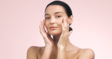 Yüzüne hafifçe dokunan kusursuz, ışıl ışıl ciltli genç bir kadının yakın çekimi. Cilt bakımı, güzellik ve kişisel bakım promosyonları, sağlık ve güven iletimi için ideal.