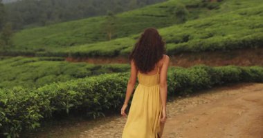Sri Lanka 'da yemyeşil çay tarlalarıyla çevrili kırsal bir patika boyunca uçan sarı elbiseli bir kadının görüntüsü. Seyahat, yaşam tarzı, doğa ve turizm promosyonları için ideal.