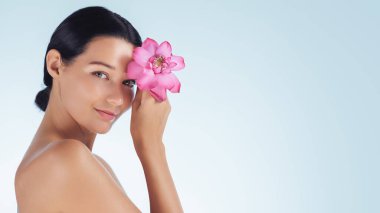 Yüzünde pembe bir nilüfer çiçeği tutan parlak derili güzel bir kadın. Reklam ve tanıtım için afiş yeri olan yüksek kaliteli kavramsal güzellik, spa ve cilt bakımı.