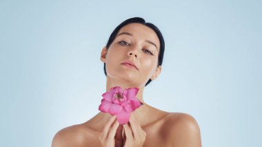 Zarif bir kadın boynunda pembe bir nilüfer çiçeği tutuyor doğal güzellik ve cilt bakımını vurguluyor. Spa, sağlık, güzellik tedavisi ya da organik kozmetik ürün reklamları için mükemmel..