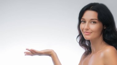 Çekici, beyaz tenli, gülümseyen ve elini uzatan beyaz bir kadın. Cilt bakımı, güzellik, kozmetik veya ürün sunumu için ideal.