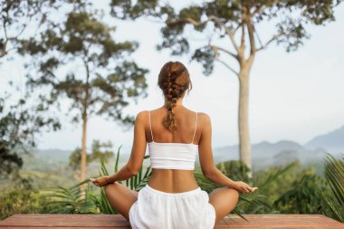 Genç bir kadın, Tayland, Krabi 'de meditasyon yapıyor. Etrafı tropik ağaçlar ve dağ manzaralarıyla çevrili. Sağlık, yoga, kişisel bakım ve eko-yaşam tarzı içerik oluşturma için harika.