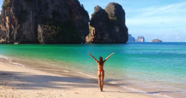 Kırmızı bikinili genç bir kadın Tayland 'daki Phra Nang Sahili' nde poz veriyor ve oynuyor. Tertemiz suları olan egzotik bir yer, promosyon, seyahat, güzellik ve yaşam tarzı kavramları için ideal..