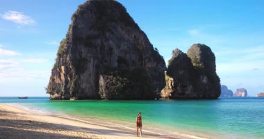 Kırmızı bikinili beyaz kadın, arka planda Ko Rang kayalıkları olan Krabi Phra Nang Sahili 'nde yalınayak yürüyor. Reklam ve seyahat reklamları için tropik güzelliği, özgürlüğü ve yaşam tarzını yakalıyor..