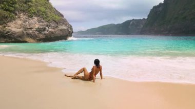 Bikini 'li kadın Kelingking Sahili' nin kıyılarında dinleniyor, Nusa Penida, Bali, su dalgaları köpürüyor, seyahat kampanyaları, spa ve sağlık temaları, ilham verici sahneler ve modern tropikal filmler için mükemmel.