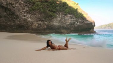 Kuma bulanmış kırmızı bikinili bir kadının, Kelingking Sahili 'nde, Nusa Penida, Bali' de eğlenceli bir şekilde poz vermesi. Otel tanıtımları, sosyal medya ve tropikal yaşam tarzı için mükemmel..