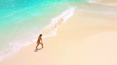 Yüksek kaliteli insansız hava aracı görüntüleri, seyahat kampanyaları, sağlık temaları, tatil beldeleri ve modern yaşam tarzı video kavramları için ideal bir plajda gezinen bir kadını yakalıyor..