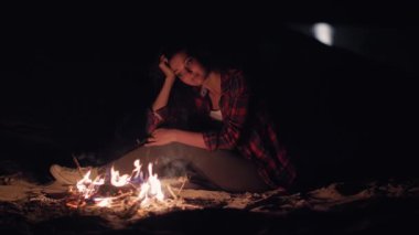 Genç bir kadın geceleri sahilde kamp ateşinin yanında oturur, düşünceli bir şekilde alevlere bakar. Huzurlu atmosfer, ateşin sıcaklığı ile, rahat, yansıtıcı bir ruh hali yaratır yolculuk için mükemmel.