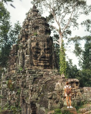 Yalnız bir sırt çantalı Kamboçya 'daki Khmer tapınağının duvarına kazınmış kocaman bir yüze bakar. Ormanla çevrelenmiş olan sahne, miras, gizem ve tek kişilik macera titreşimleri taşır..