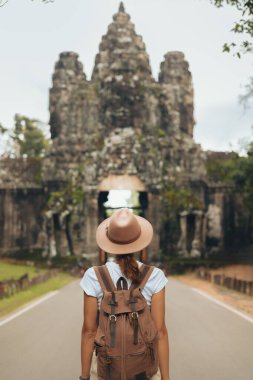 Angkor Thom kapısı ve Bayon yüz kuleleri yolda duran şapkalı bir bayan sırt çantalı kadim girişi hayranlıkla izliyor. Reklamlar, bloglar ve Kamboçya turizmi için yüksek kaliteli seyahat imajı.