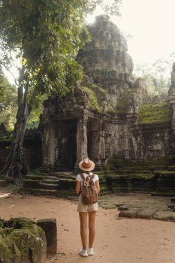Yosunlu Angkor kapısındaki dişi sırt çantası orman ağaçlarının altında duruyor, sıcak ışıkta yakalanmış. Konsept, seyahat reklamcılığı, kültür turizmi, bloglar ve miras eğitimi için yüksek kaliteli yazı işleri.