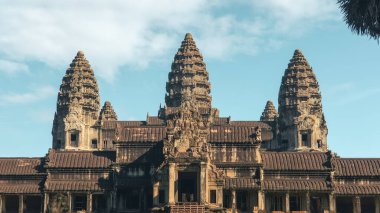 Öndeki Angkor Wat cephesinde beş Khmer kulesi, kumtaşı galerileri ve parlak bir gökyüzünün altındaki gölgeler sergileniyor. Seyahat editörleri ve turizm kampanyaları için uygun kavramsal ve yüksek kaliteli imaj.
