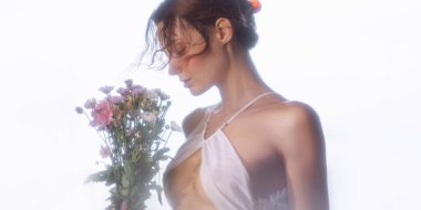 Yumuşak ışıkta taze çiçekleri tutan beyaz bir kadının şehvetli portresi. Güzellik, kadınlık, sağIık veya romantik tanıtım kullanımı için kavramsal, yüksek kaliteli stok imajı.