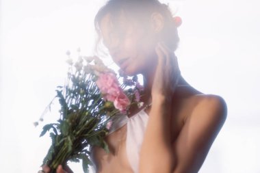 Bulanık, yumuşak bir ışıkta elinde bir buket çiçek tutan bir kadının şehvetli görüntüsü. Güzellik, romantizm, reklam, spa, doğa ya da yayın kampanyaları için ideal kavramsal ve sanatsal fotoğraf.