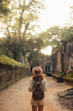 Kamboçya 'daki Angkor tapınağının taş koridorunda yürüyen sırt çantası ve şapkalı kadın gezgin seyahat blogları, turizm reklamları, tarih temaları ve ilham verici macera içerikleri için ideal.. 