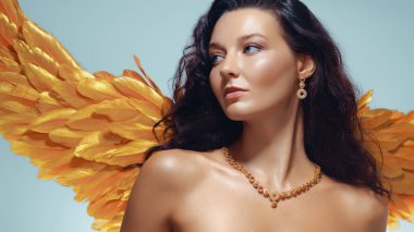 Parlak tenli, zarif mücevherleri ve altın melek kanatları olan, moda, güzellik, fantezi, reklam ve yaratıcı projeleri için mükemmel, yüksek kalite kavramsal bir kadın portresi..