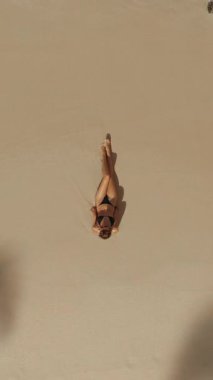 Kadının tropikal kumlu sahilde güneşlenirken çekilmiş, hafif dalgalar, lüks seyahatler, refah ve yaz tatili temaları, turizm reklamları, tatil beldeleri, markalar ve