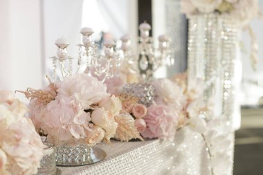 Lüks düğün masası allık rengi şakayık süslemeler, kristal şamdanlar ve yumuşak ışıkta parlayan çarşaflarla süslenmiş. Zarif etkinlikler, tanıtım reklamları, afişler ve kutlama markaları için konsept görüntü