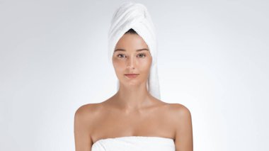 Kafasında havluyla parlayan cildi olan genç bir kadın sakin ve rahat görünüyor. Doğal güzelliği ve sağlıklı teni spa, cilt bakımı ve kişisel bakım promosyonları için ideal bir konsept oluşturuyor..