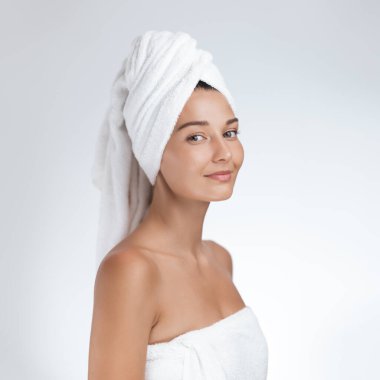 Işıl ışıl cildi yumuşak beyaz bir havluya sarılı, taze yüzlü bir kadın. Nazikçe gülümsüyor. Güzelliği, kendine bakımı ve cilt bakımını temsil ediyor. Sağlıklı ve parlak ciltler için..