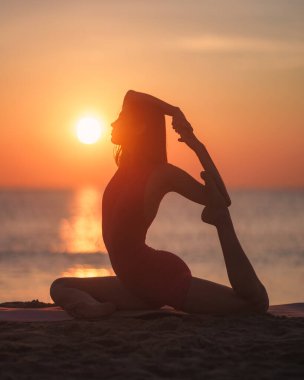 Sahilde yoga yapan, arka planda batan güneşi olan bir kadının silueti. Farkındalık, açık hava fitness ve dinginlik ortamları ile ilgili konular için mükemmel..