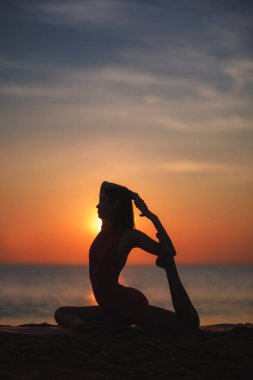 Güneş doğarken sahilde yoga yapan, siluette yakalanmış sağlıklı bir kadın. Zarif bir duruş sergiliyor, sükuneti, esnekliği ve dengeyi kucaklıyor. Sağlık ve farkındalık temaları için mükemmel..