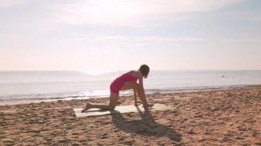 Beyaz kadın açık mavi gökyüzünün altında kumlu sahilde yoga pozu veriyor. Sağlık, zindelik ve yaşam tarzı konsepti reklamlar, tanıtım ve sağlık ilhamı için mükemmel..