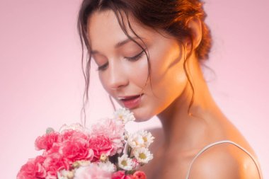 Bir buket taze pembe karanfil ve papatya tutan genç bir kadının yumuşak ve zarif portresi. Romantik güzellik kavramları, cilt bakımı, parfüm veya sağlık reklamları için idealdir..