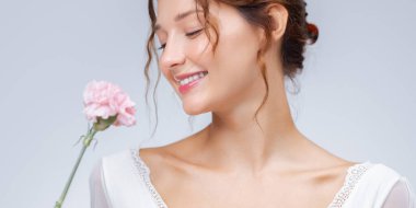 Beyaz dantel elbiseli, pembe çiçeğe gülümseyen neşeli bir kadının stüdyo güzelliği afişi. Cilt bakımında, parfüm kampanyalarında, sağlık reklamlarında ya da bahar güzellik dergilerinde kullanılmak için birebirdir..