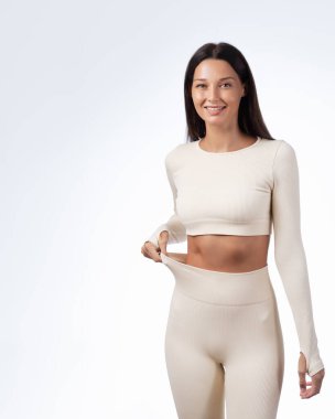 Genç, beyaz bir kadın göbeğini göstermek için bel bağlıyor. Sağlık, vücut güveni, diyet, sağlıkla ilgili promosyonlar için mükemmel bir imaj. Yumuşak ışıklandırmalı stüdyo çekimi.