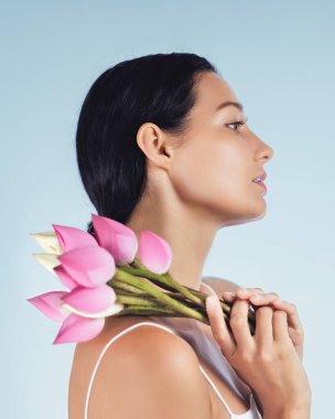 Yan profildeki zarif kadın omzunda doğal güzellik ve cilt bakımını sembolize eden pembe nilüfer tomurcukları tutuyor. Spa tedavileri, sağlık promosyonları, güzellik ürünleri için ideal.