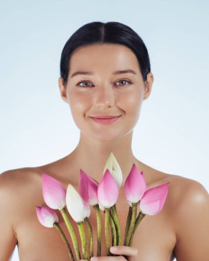 Pembe nilüfer çiçekleri tutan parlak doğal ciltli genç bir kadının yakın plan portresi. Yüksek kaliteli kavramsal güzellik görüntüsü spa, cilt bakımı, kozmetik, sağlık ve yaşam tarzı tanıtımı için mükemmeldir..